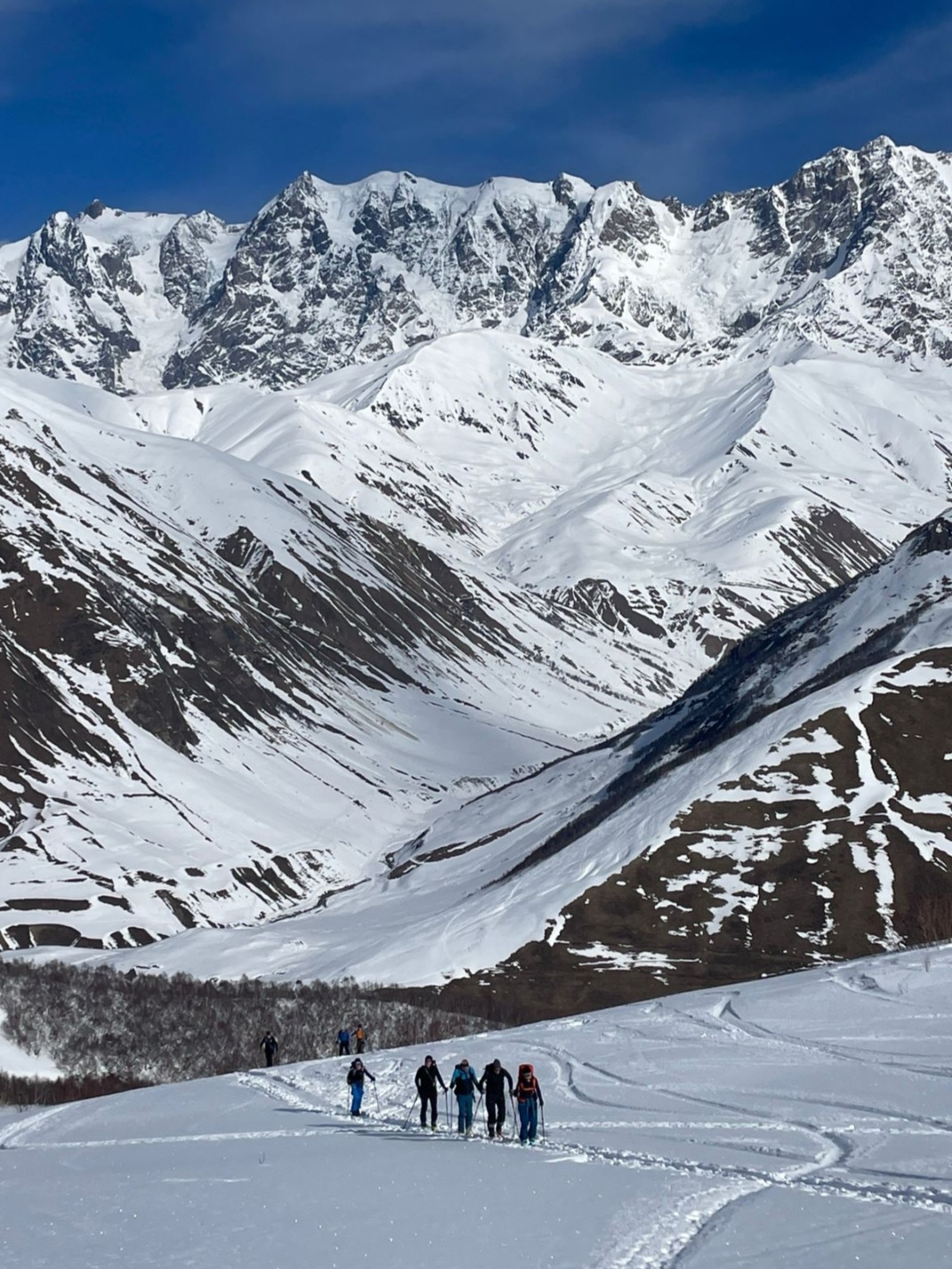 Ski tourers skinning up a snow slope beneath the high Caucasus wall on the way to Ushguli, Upper Svaneti