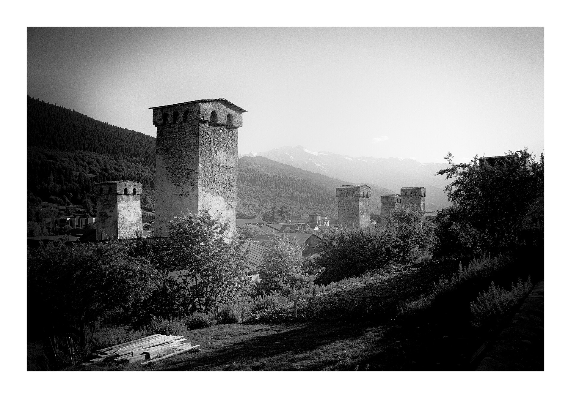 Black and white photograph of Svan stone towers in Mestia with the Caucasus range behind